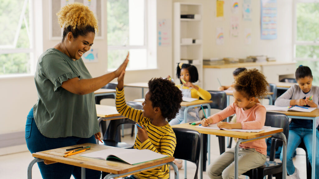 Teacher high-fiving student sitting in desk.