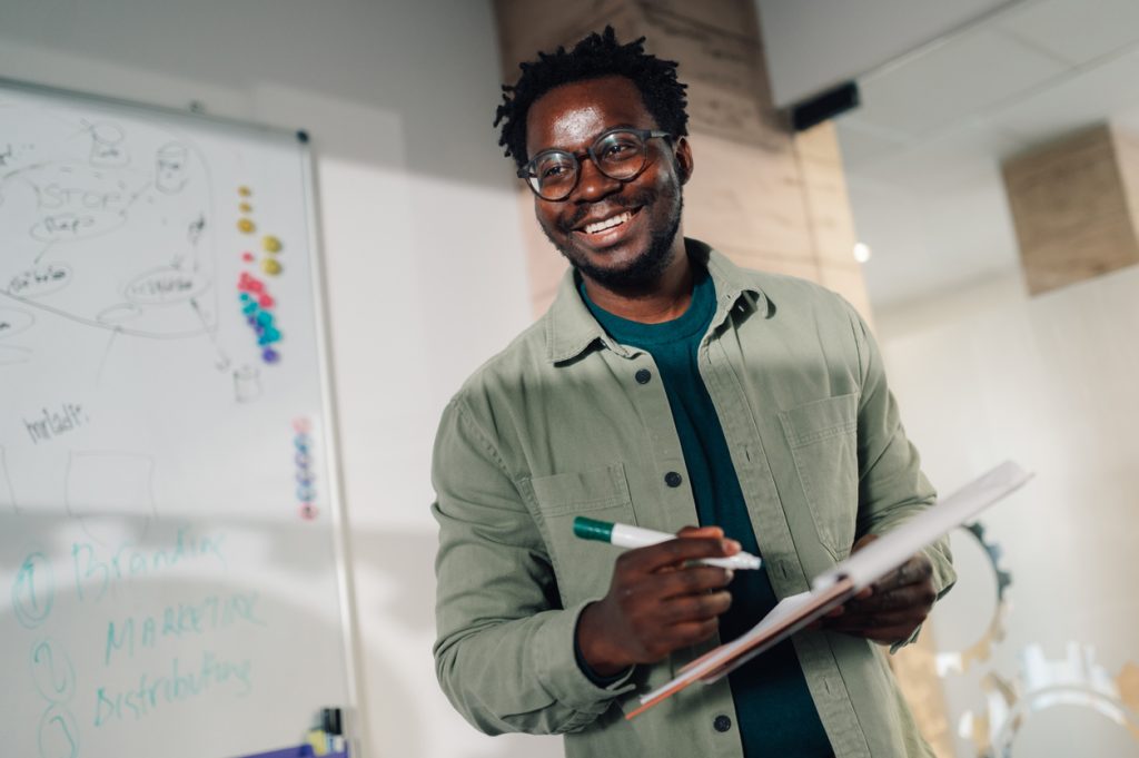 Smiling man holding notebook and marker in office meeting room